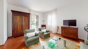 Una sala de estar con dos sillones, un aparador de madera, un televisor y una mesa de centro de vidrio.