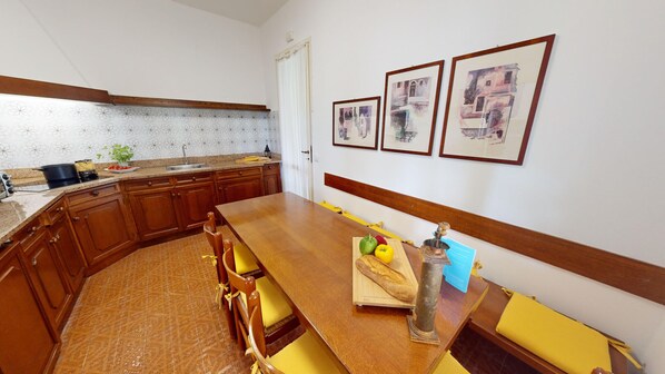 Una cocina con armarios de madera, encimera de granito y una mesa de comedor con cojines amarillos. Hay tres cuadros en la pared.