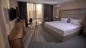 Une chambre d’hôtel avec un grand lit, un bureau, une chaise, une télévision et un balcon avec des rideaux.