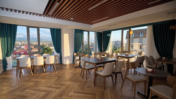 Un vaste espace dédié à la salle à manger, avec de nombreuses tables et chaises, de grandes fenêtres dotées de rideaux et un plancher en bois.
