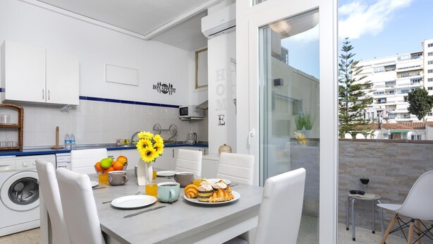 Een moderne keuken met witte kasten, een eethoek met een tafel gedekt voor twee personen, en uitzicht op een woongebouw door een glazen deur.