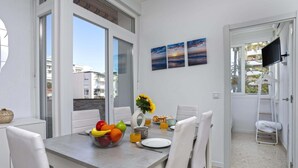 Een eethoek met een tafel gedekt voor twee personen, een fruitschaal, een vaas met zonnebloemen en een schilderij aan de muur.
