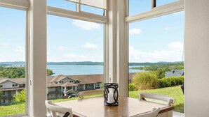 A dining area with a table and chairs, large windows with a view of a lake and surrounding buildings. - Lake View Condo with 2 K Beds, Golf & Ticket Discounts! (Branson)