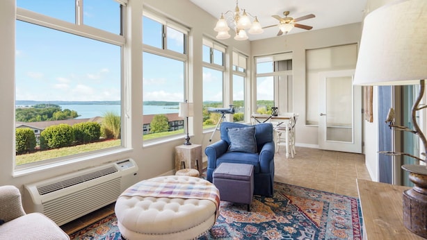 A spacious room with large windows, a comfortable seating area, a ceiling fan, and a view of the outdoors. - Lake View Condo with 2 K Beds, Golf & Ticket Discounts! (Branson)