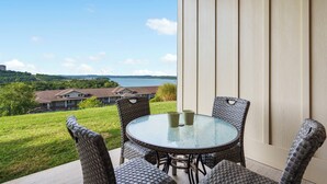 A patio with wicker chairs and a glass table, overlooking a lake and houses. - Lake View Condo with 2 K Beds, Golf & Ticket Discounts! (Branson)