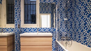 A bathroom with a geometric blue and white tile pattern, a wooden vanity, a white sink, and a glass-enclosed shower area. - Tiny House St Germain /AC (Paris)
