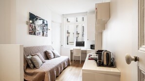 A compact living space with a sofa, a small desk, a kettle, and a door. - Tiny House St Germain /AC (Paris)