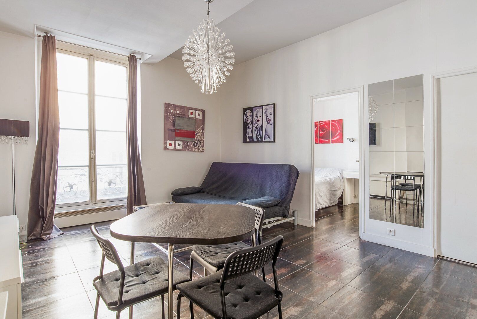 Uma sala de estar moderna com uma mesa de jantar redonda, duas cadeiras, um sofá e um candelabro.