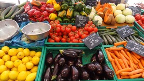 Een kraam op een markt met diverse groenten zoals tomaten, wortels en aubergines, elk voorzien van een prijslabel.