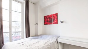 Een slaapkamer met een bed, een raam met gordijnen en een kunstwerk aan de muur.