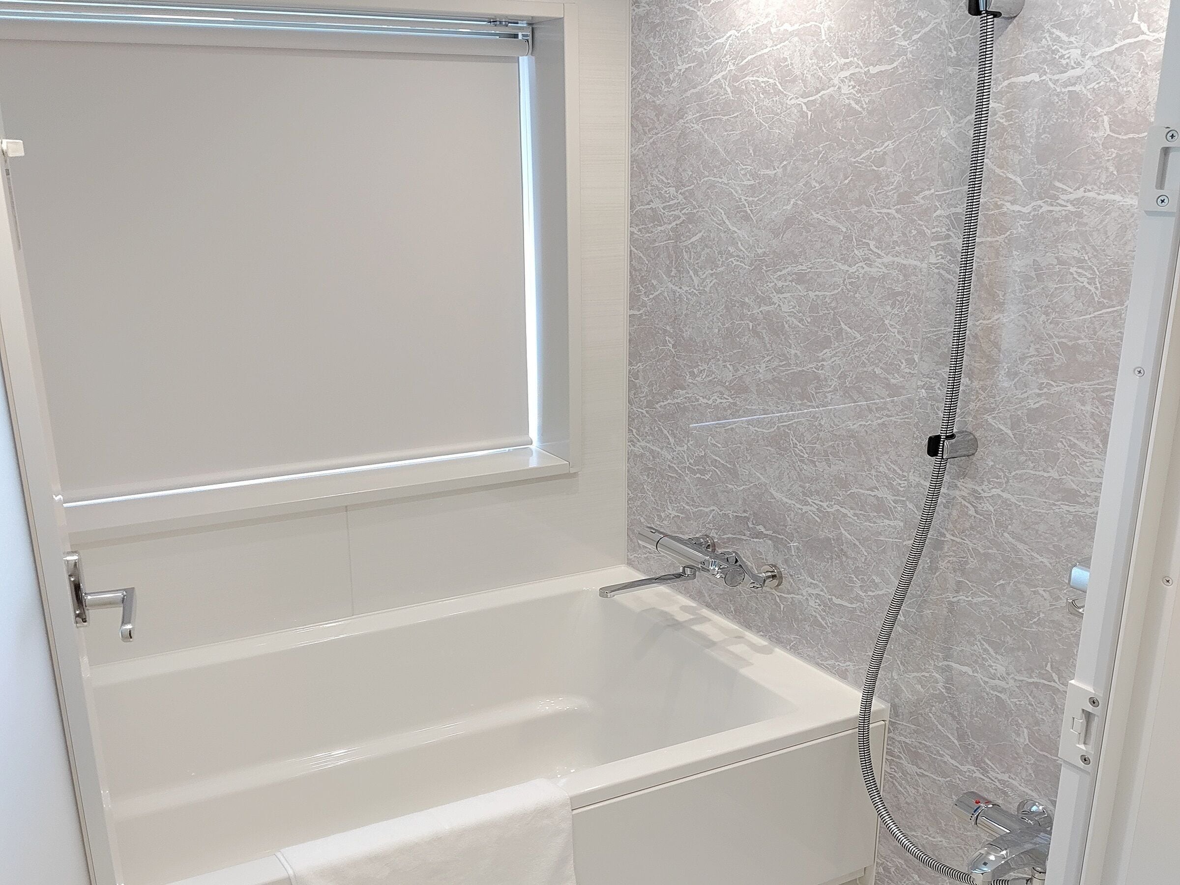 A modern bathroom with a bathtub, a shower, and marble walls.