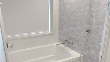 A modern bathroom with a bathtub, a shower, and marble walls.