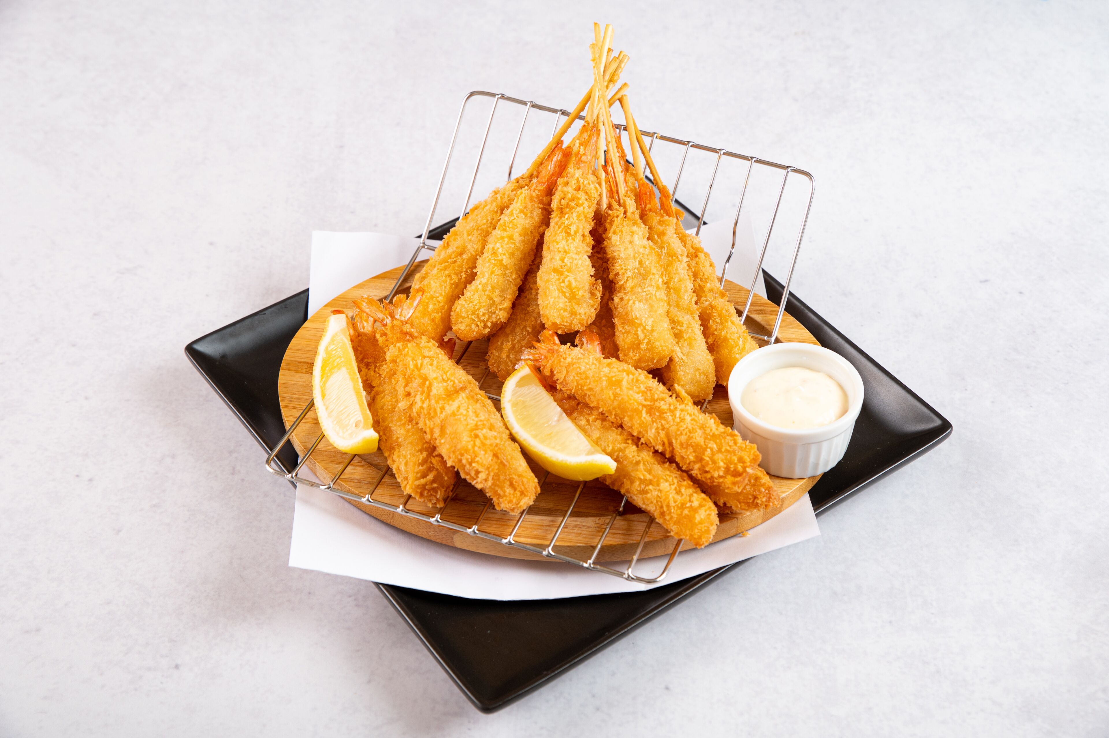 A tray of breaded and fried shrimp on a wire rack with lemon wedges and a small bowl of dipping sauce.