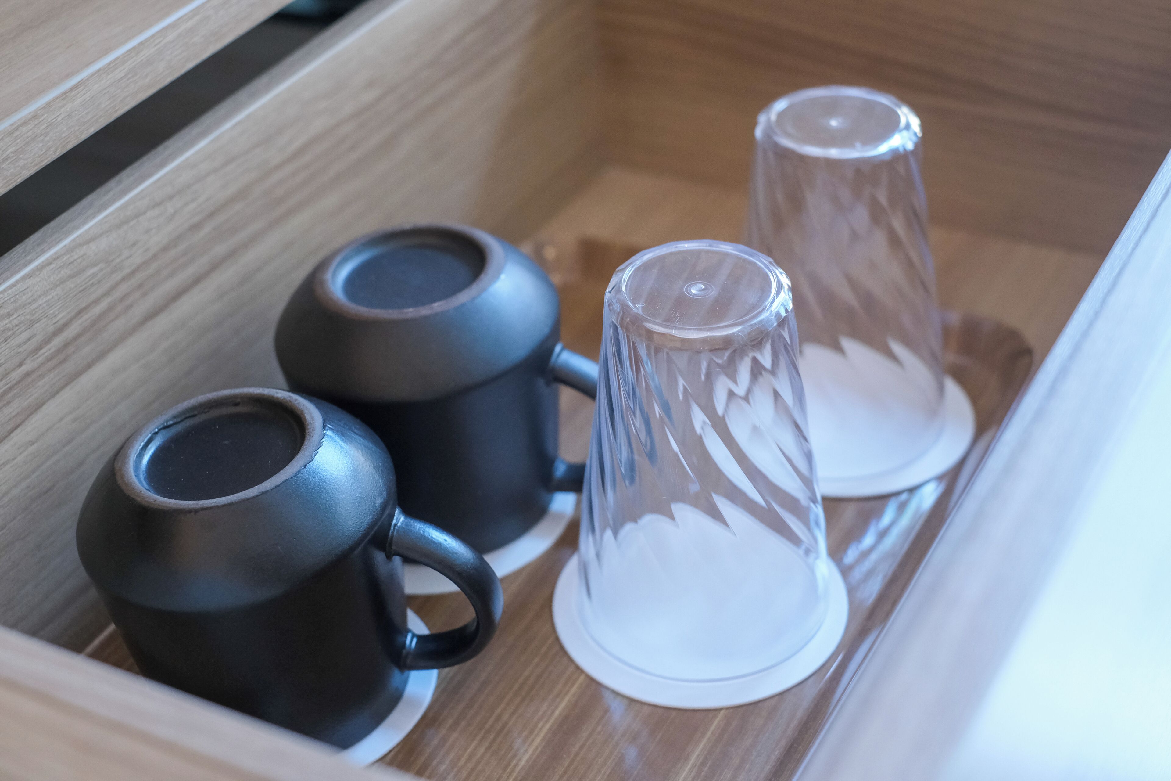 Un cajón de madera con dos tazas negras y dos vasos de vidrio transparente con tapas.