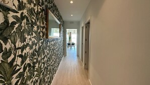 A hallway with a patterned wallpaper, a wooden floor, and a mirror on the left wall.