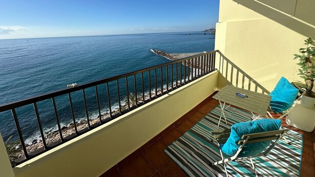 A balcony with a view of the ocean, a tiled floor, and a chair with a cushion.