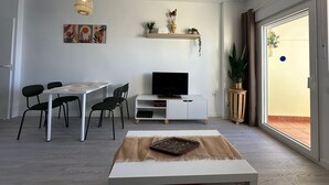 A modern living room with a dining area, a flat-screen TV, and a large sliding glass door to the outside.