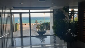 A modern hotel lobby with a glass door leading to a balcony overlooking the sea.