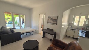 A modern living room with a sofa, a small round table, and a dining table. There is a kitchen area with a microwave and a sink. - Petite Maison en Pleine Nature Avec Piscine (Puget-sur-Argens)