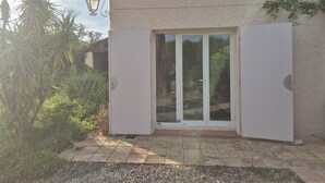 A house with a white exterior, a tiled patio, and a sliding glass door. - Petite Maison en Pleine Nature Avec Piscine (Puget-sur-Argens)