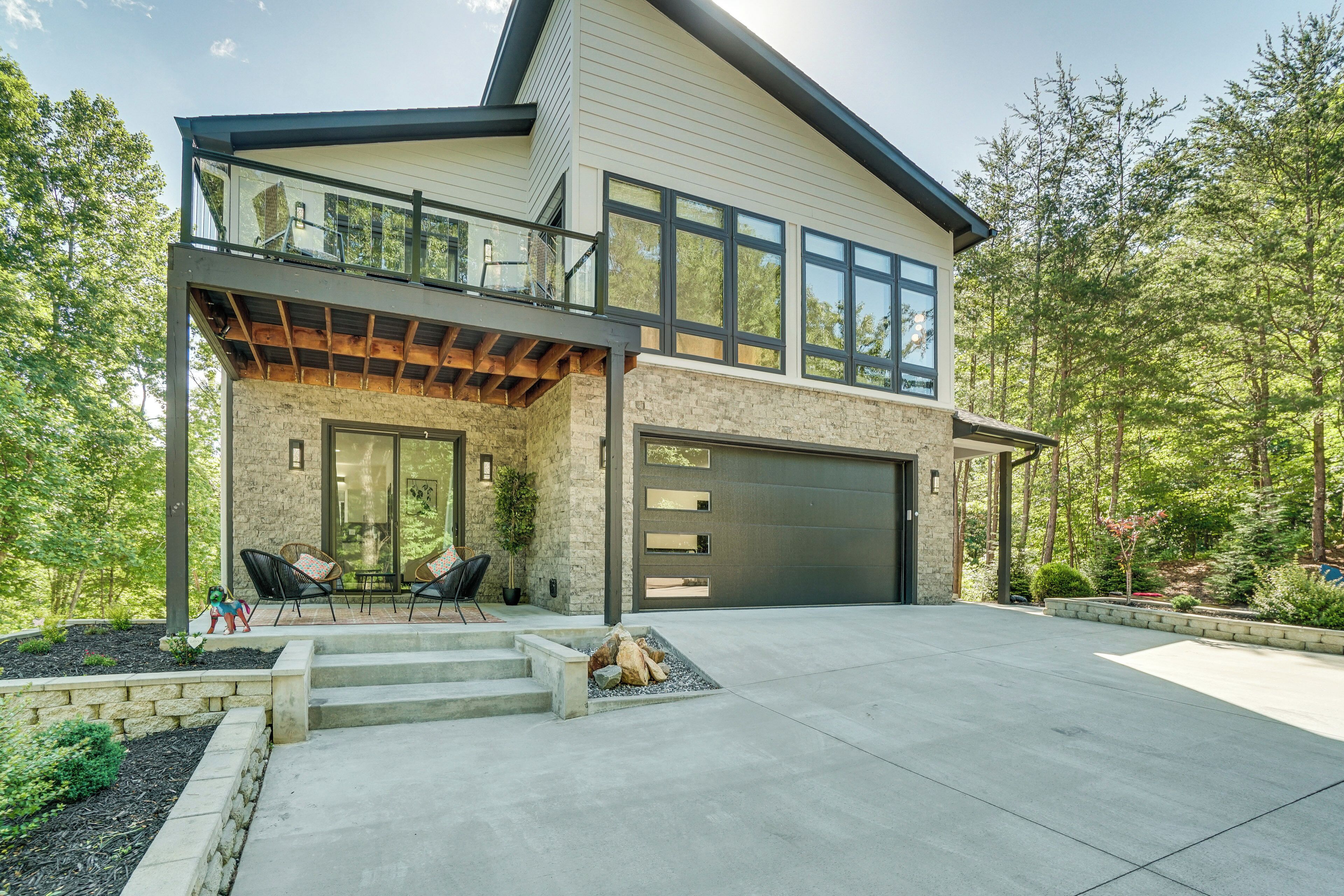 A modern two-story house with a large garage, a covered patio with outdoor furniture, and a stone facade.
