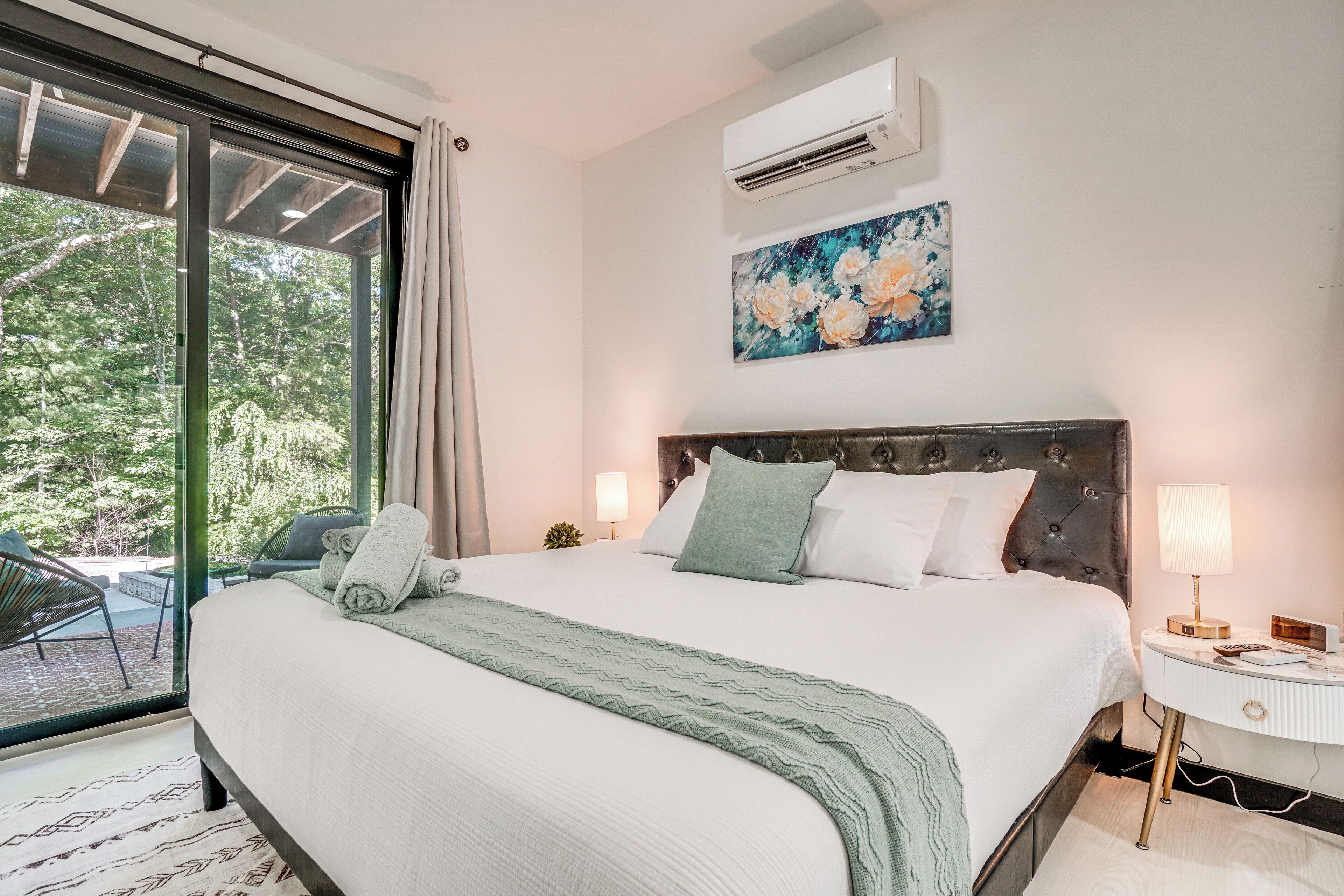 A bedroom with a large bed, a nightstand, a lamp, and a painting on the wall.