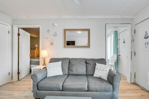Une pièce avec un canapé gris, un miroir à cadre en bois, une porte blanche et une petite table avec une lampe.
