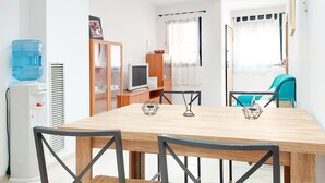 Ein Essbereich mit einem Holztisch, vier Stühlen, einem Wasserspender, einem Fernseher und einer Vitrine.