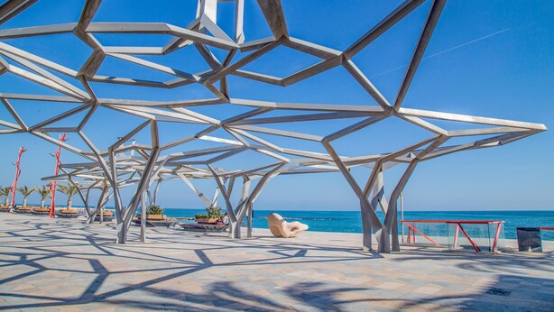 Eine geometrische Metallkonstruktion mit freiem Blick auf das Meer und einem gefliesten Weg.
