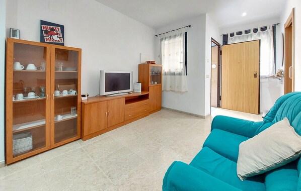 Una sala de estar con un sofá azul verdoso, armarios de madera con puertas de vidrio, un televisor y un cartel en la pared.