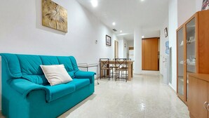 Ein Wohnzimmer mit einem türkisfarbenen Sofa, einem Esstisch mit Stühlen und einem Holzschrank.