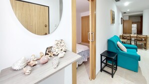 Ein Wohnzimmer mit einem türkisblauen Sofa, einem Holztisch mit dekorativen Muscheln, einem runden Spiegel und einem hölzernen Kleiderschrank.