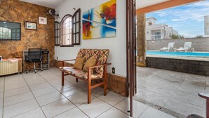 Ein Zimmer mit einer Couch, einem Schreibtisch, einem Stuhl, einem Gemälde und Blick auf einen Swimmingpool.