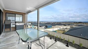 Een balkon met een glazen tafel, een barbecue en uitzicht op een woonwijk.