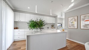 Una cuina moderna amb armaris blancs, una illa central i una planta en test.