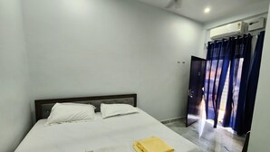 A hotel room with a bed, a ceiling fan, an air conditioning unit, and a view through a curtain. - Raghubir Nikunj Homestay (Faizabad)