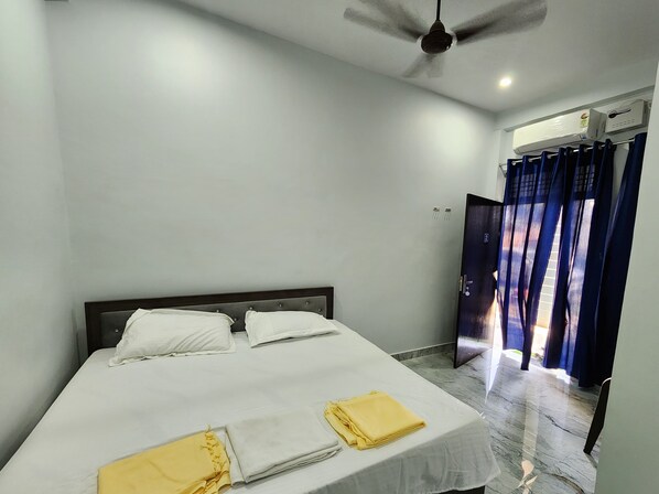 Habitación de hotel con cama, ventilador de techo, equipo de aire acondicionado y vistas a través de una cortina.