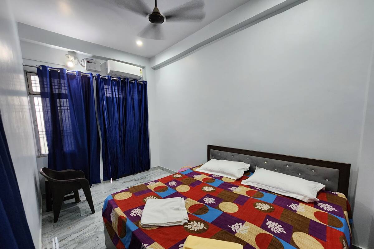 A bedroom with a bed, a chair, a ceiling fan, and a window with curtains.