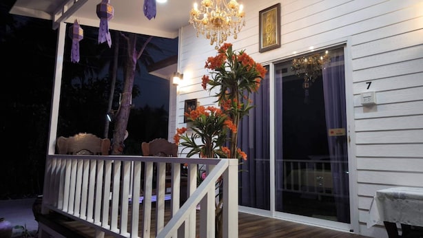 Eine Veranda mit weißem Geländer, einer Bank, einem Kronleuchter und einem Blumentopf mit orangen Blüten.