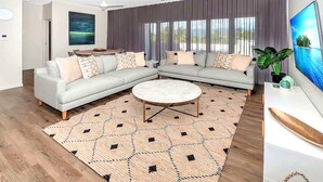 A modern living room with a sectional sofa, a round coffee table, and a large window with curtains.