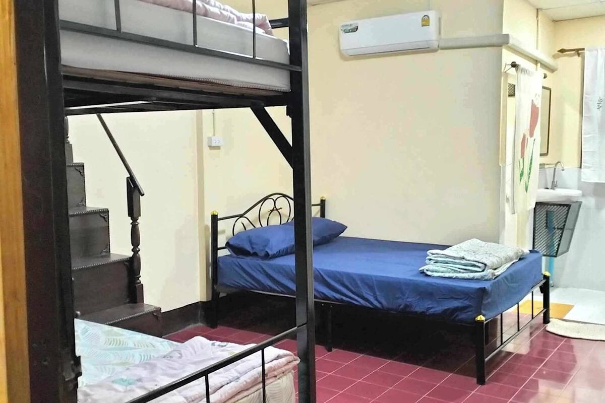 A dormitory room with bunk beds, a desk, and a bathroom with a sink and mirror.