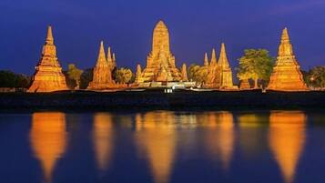 A temple complex with multiple structures, including a central large temple and smaller ones on either side, all illuminated and reflecting on the water in front.