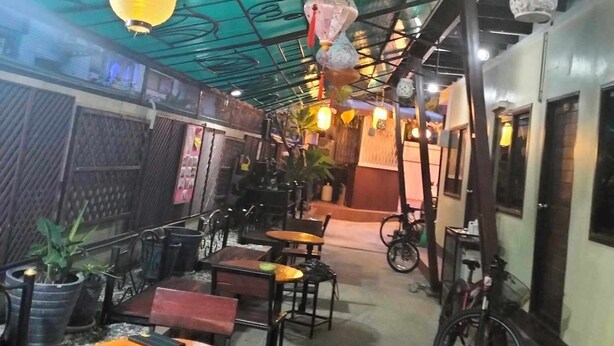 An indoor dining area with tables and chairs, hanging lanterns, and a bicycle parked against the wall. - V House (Ayutthaya)