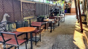 A narrow outdoor café area with tables and chairs, a decorative wall, and a statue. - V House (Ayutthaya)