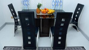 Un comedor con una mesa de vidrio, sillas negras y una cesta de frutas que contiene piña, manzanas, naranjas y plátanos.