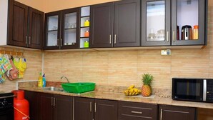 Una cocina con armarios marrón oscuro, salpicadero de azulejos, estufa a gas, microondas y un lavamanos verde.