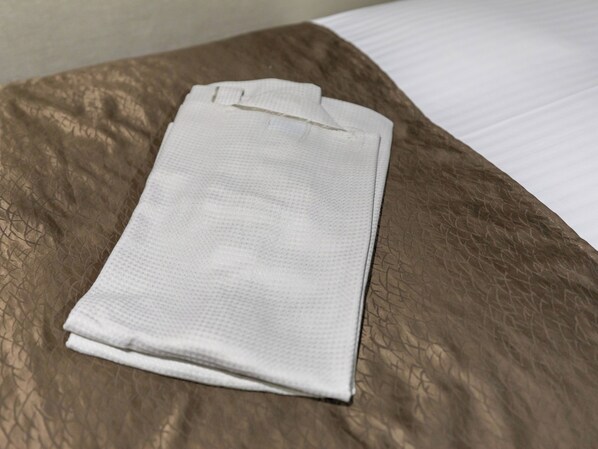 Una toalla blanca doblada con cuidado sobre una colcha marrón con textura.