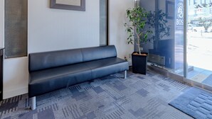 A reception area with a black leather bench, a potted plant, and a glass door leading outside. - Tabist Takamatsu Pearl Hotel (Takamatsu)