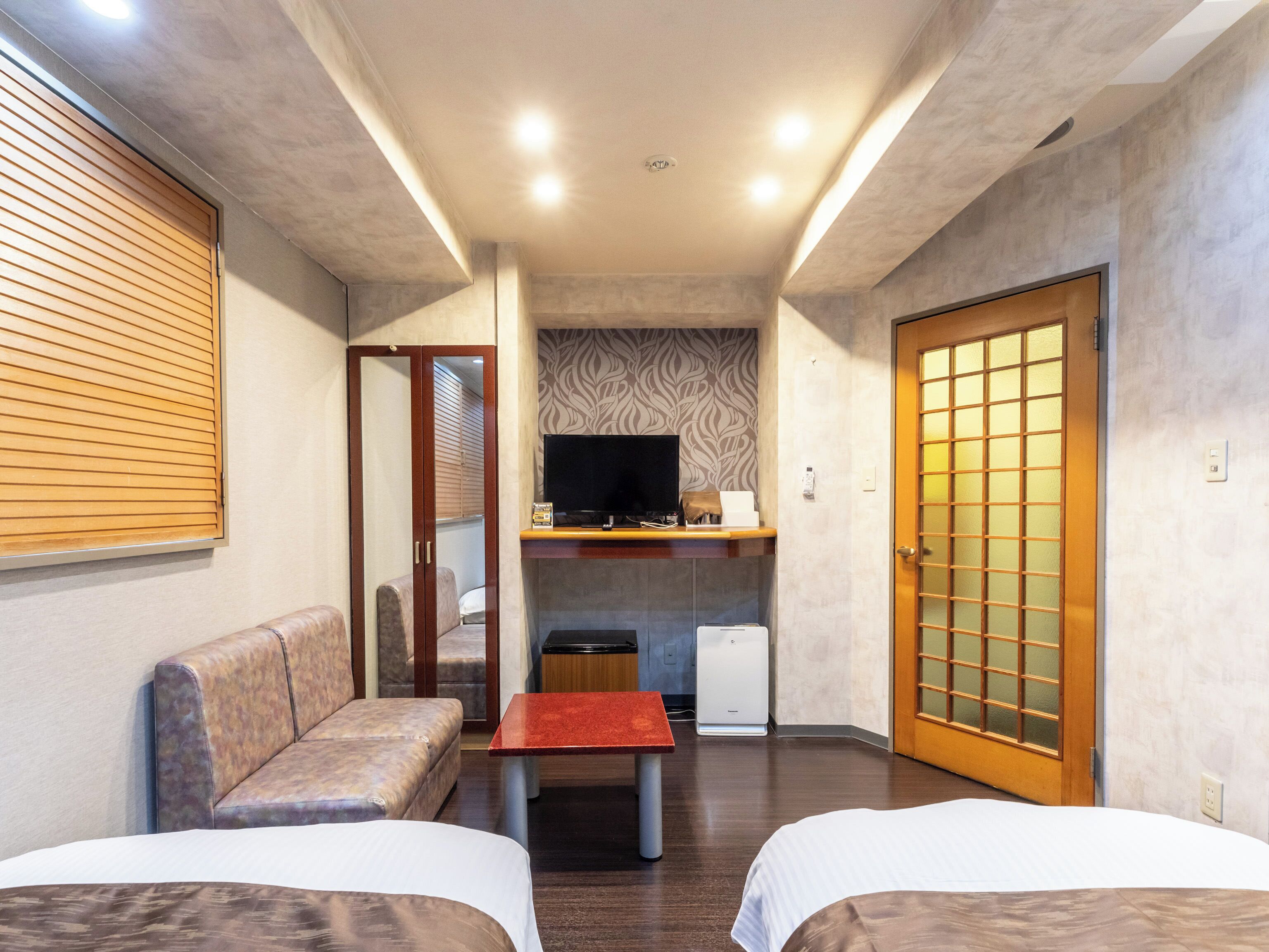 A hotel room with a sofa, a small table, a TV, and a cabinet.