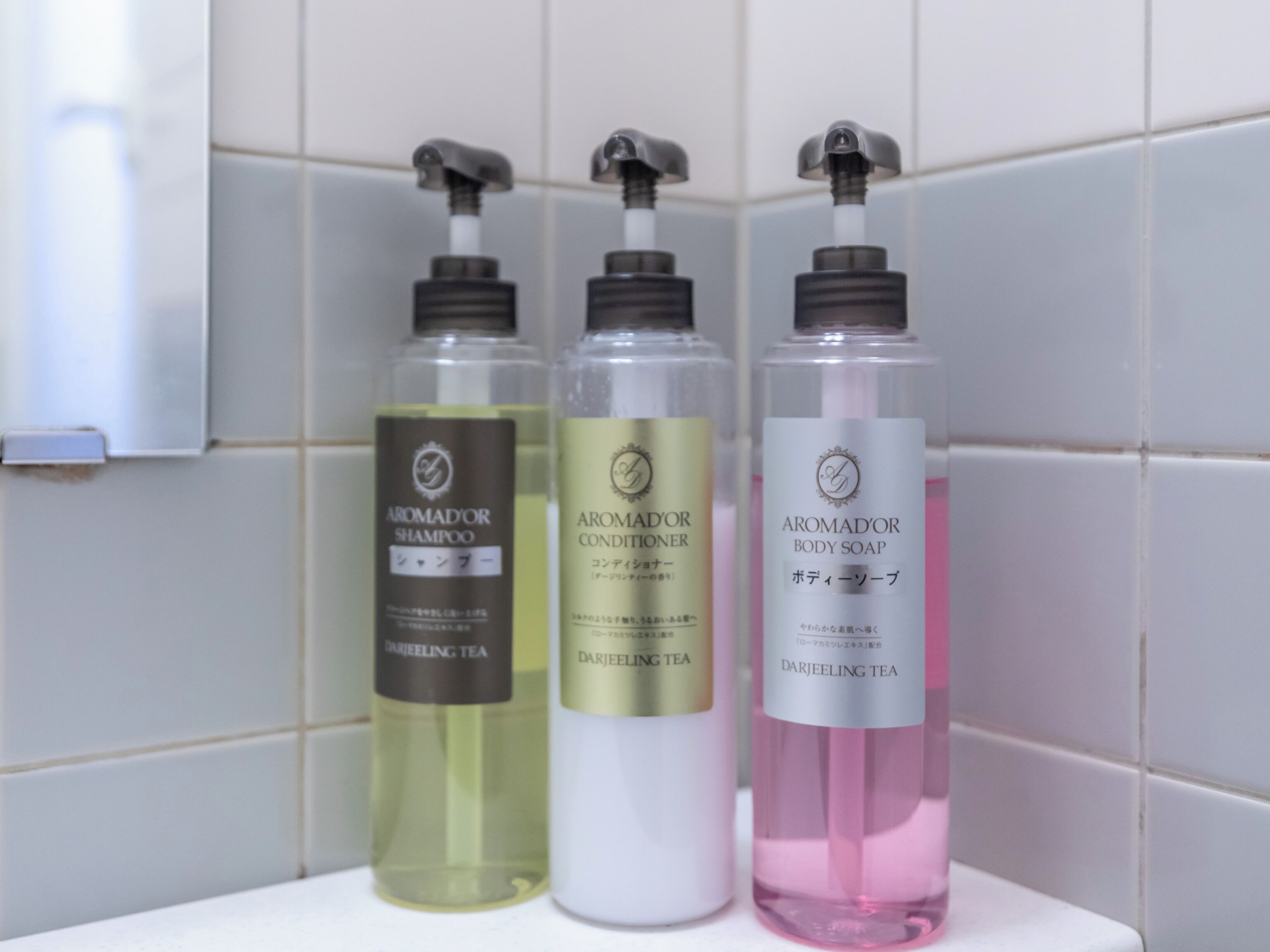 Three bottles of Aromador products on a white surface against a tiled wall.